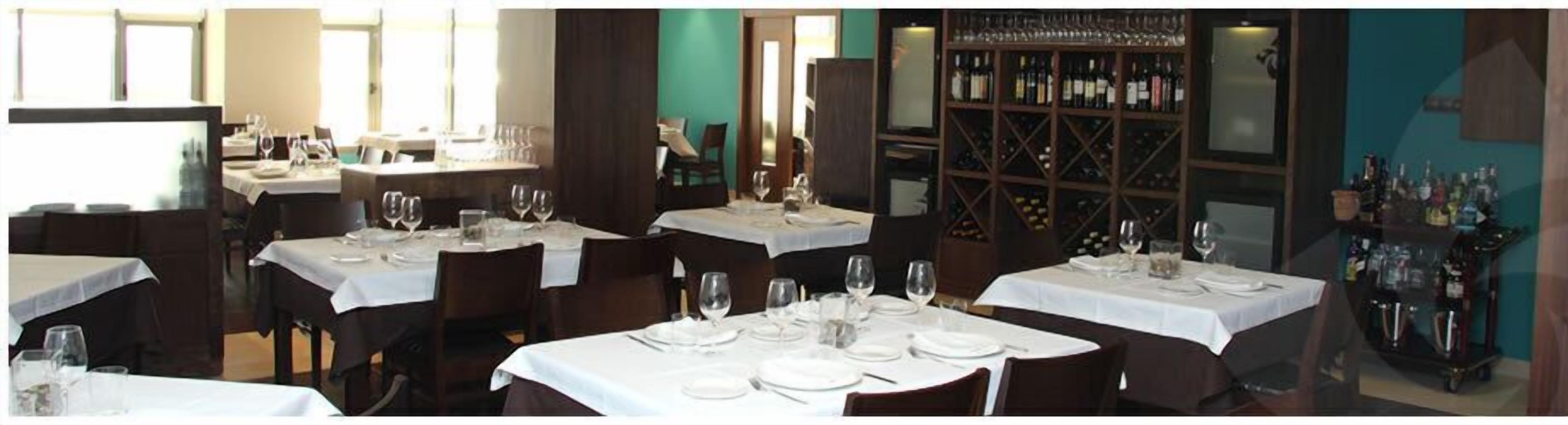 Un restaurant avec de nombreuses tables dressées pour le dîner, chacune étant recouverte d’une nappe blanche et agrémentée de verres à vin.