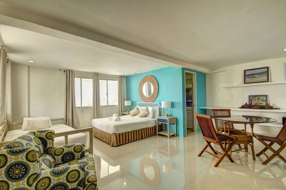 A hotel room with a bed, a desk, chairs, a mirror, and a window.