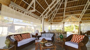 A covered outdoor seating area with wicker furniture, a glass coffee table, and a view of the outdoors. - Momo Beach House (Panglao)