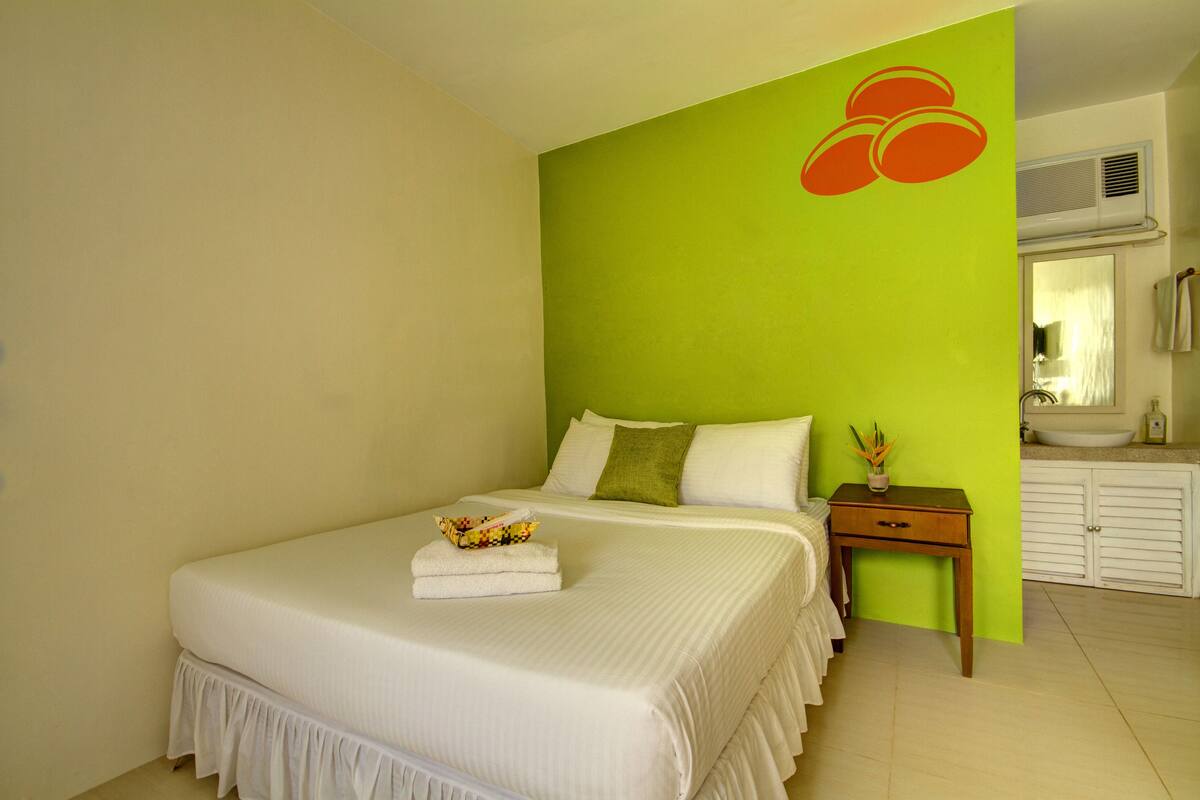 A hotel room with a large bed, a bedside table with a vase, and a green accent wall.