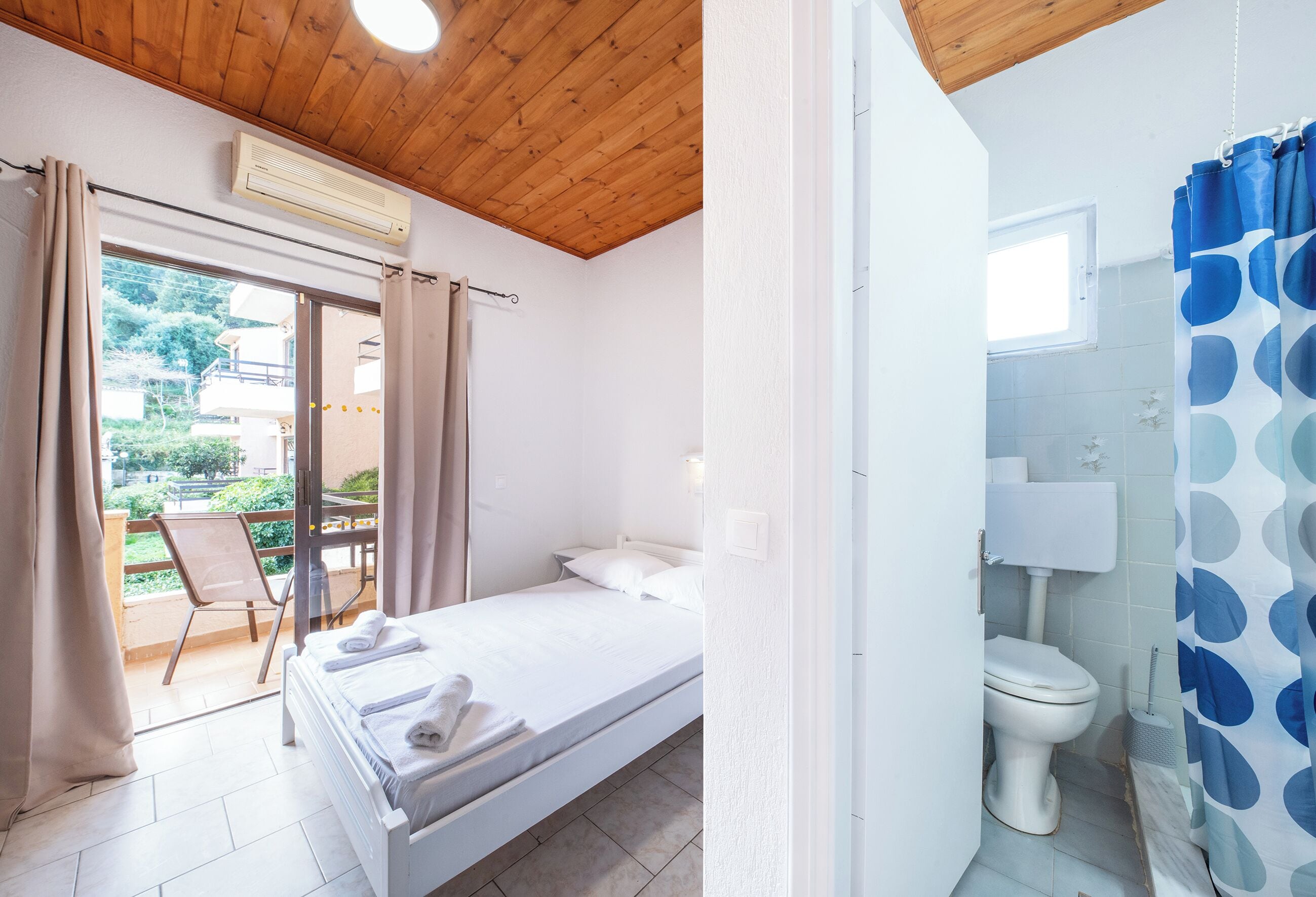 A bedroom with a bed, a chair, and a balcony with curtains.