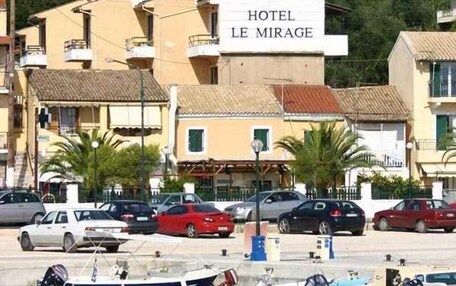 A coastal hotel named "HOTEL LE MIRAGE" with a signboard, parked cars, and boats docked at the marina.
