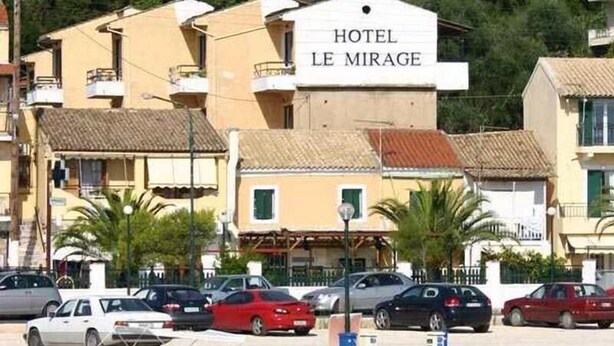 Hotel sul lungomare, denominato "HOTEL LE MIRAGE", con insegna, auto parcheggiate e barche ormeggiate al porto.