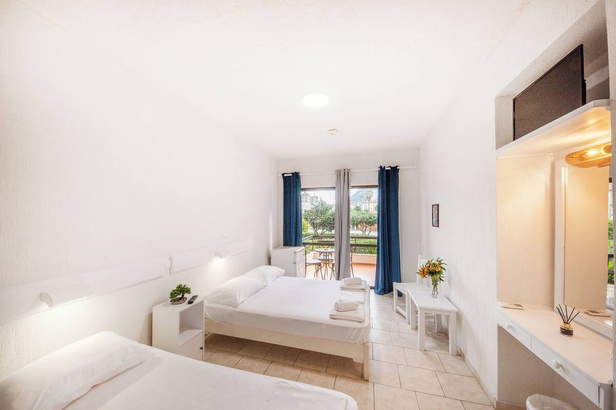 A hotel room with a bed, bedside tables, a desk, and a view of the outdoors.
