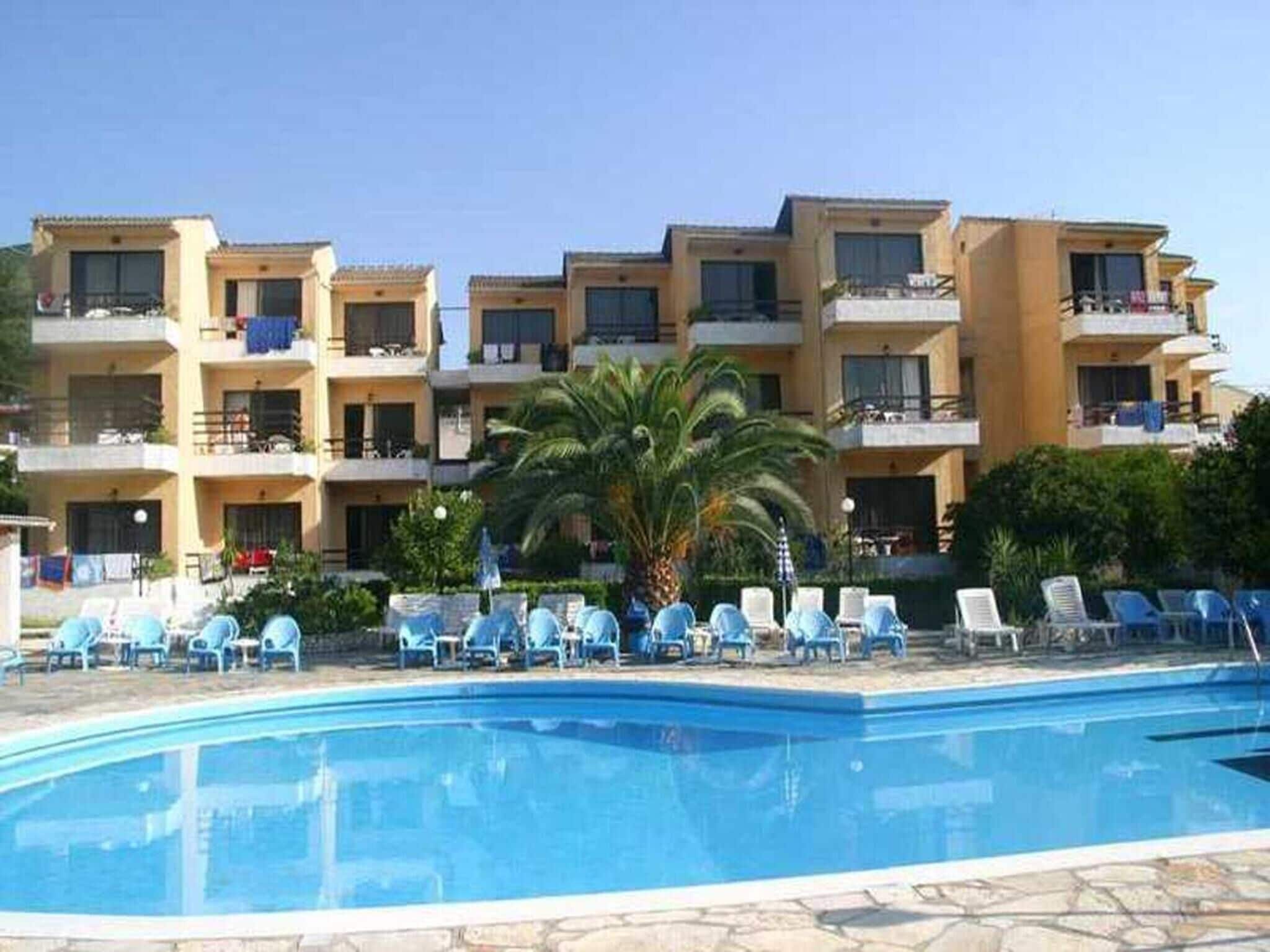 A hotel with a swimming pool, multiple balconies, and a palm tree.