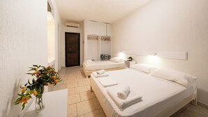 Camera d'albergo con due letti, un armadio bianco, un comodino con una lampada e un vaso con fiori.