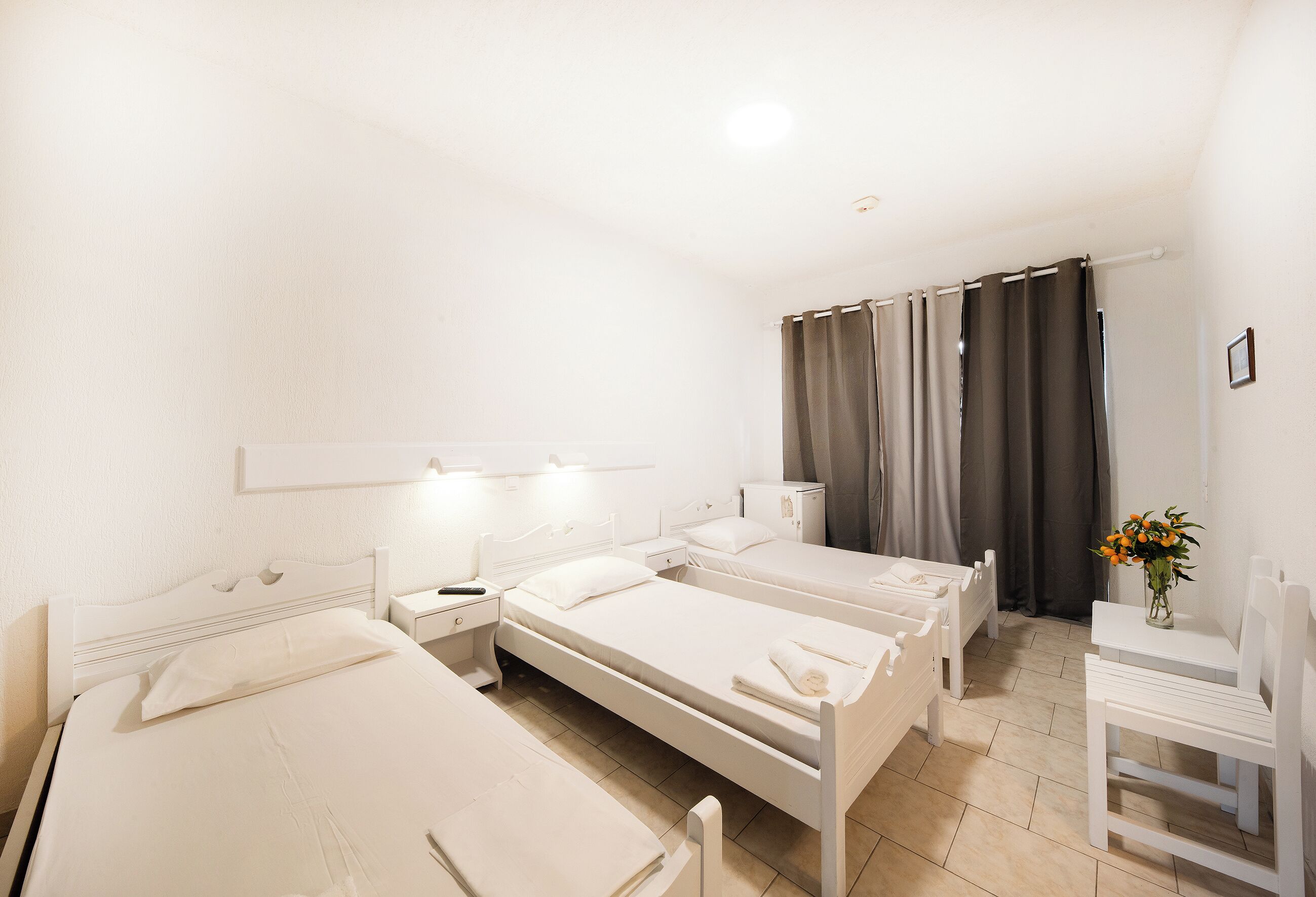 Une chambre d’hôtel avec trois lits simples, une petite table avec une chaise, un bureau et une table de chevet.
