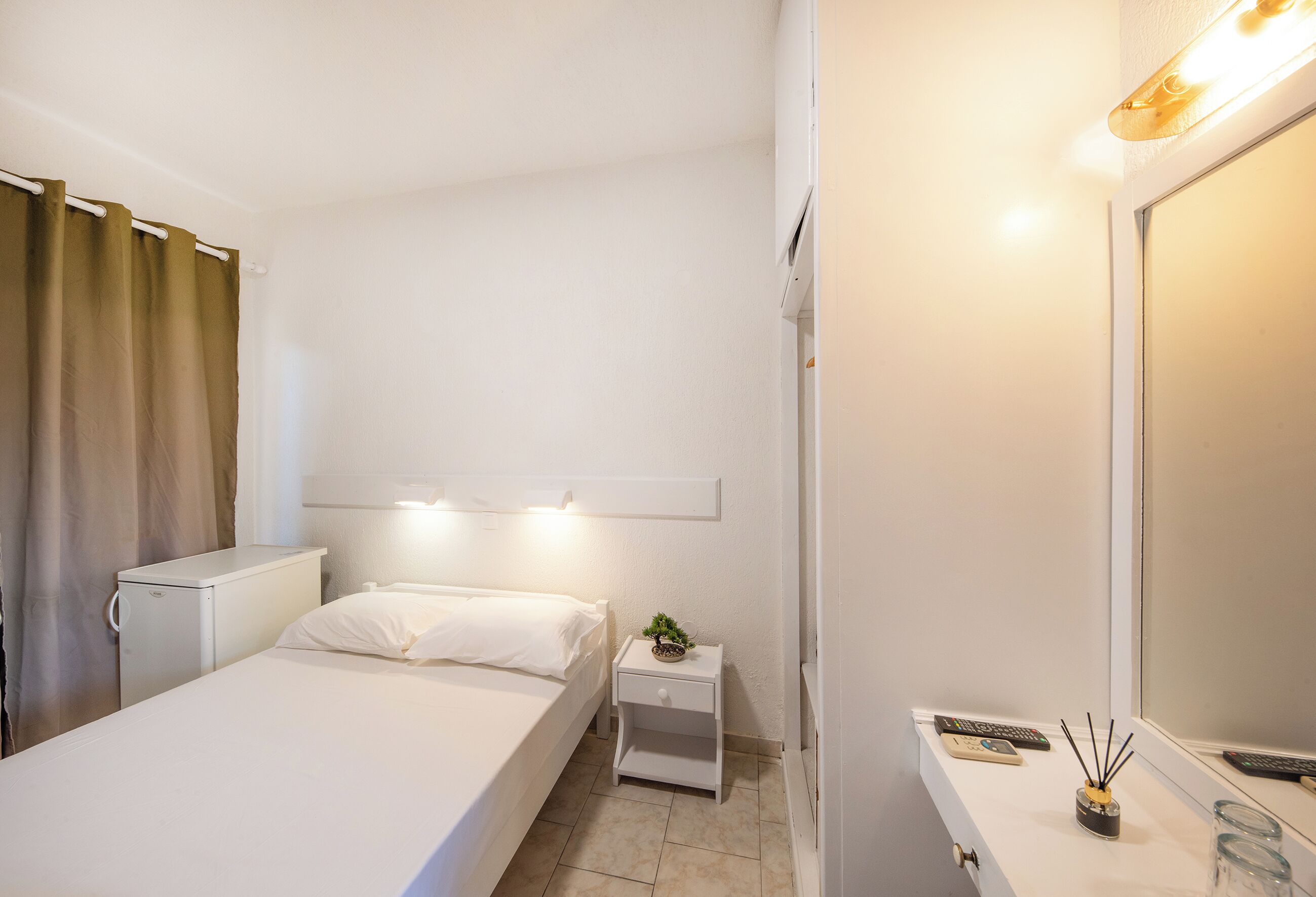 A small, clean room with a bed, a nightstand, a mirror, and a small cabinet.