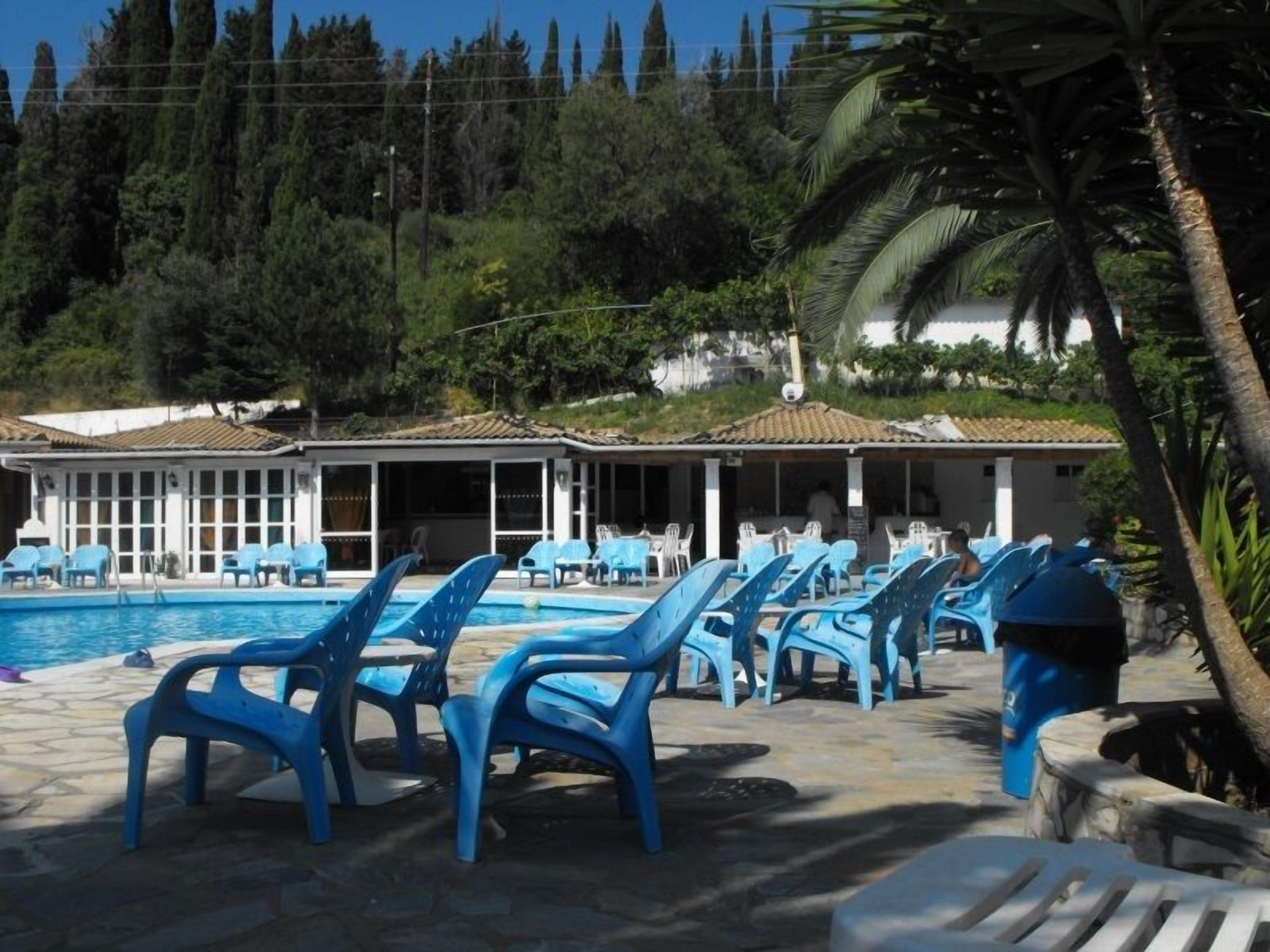 Un espace piscine avec des chaises longues bleues et un bâtiment doté d’un toit recouvert de tuiles.