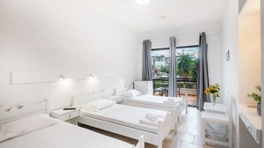 Una camera d'hotel con tre letti singoli, un tavolino con un vaso di fiori e un balcone con vista sulla città.