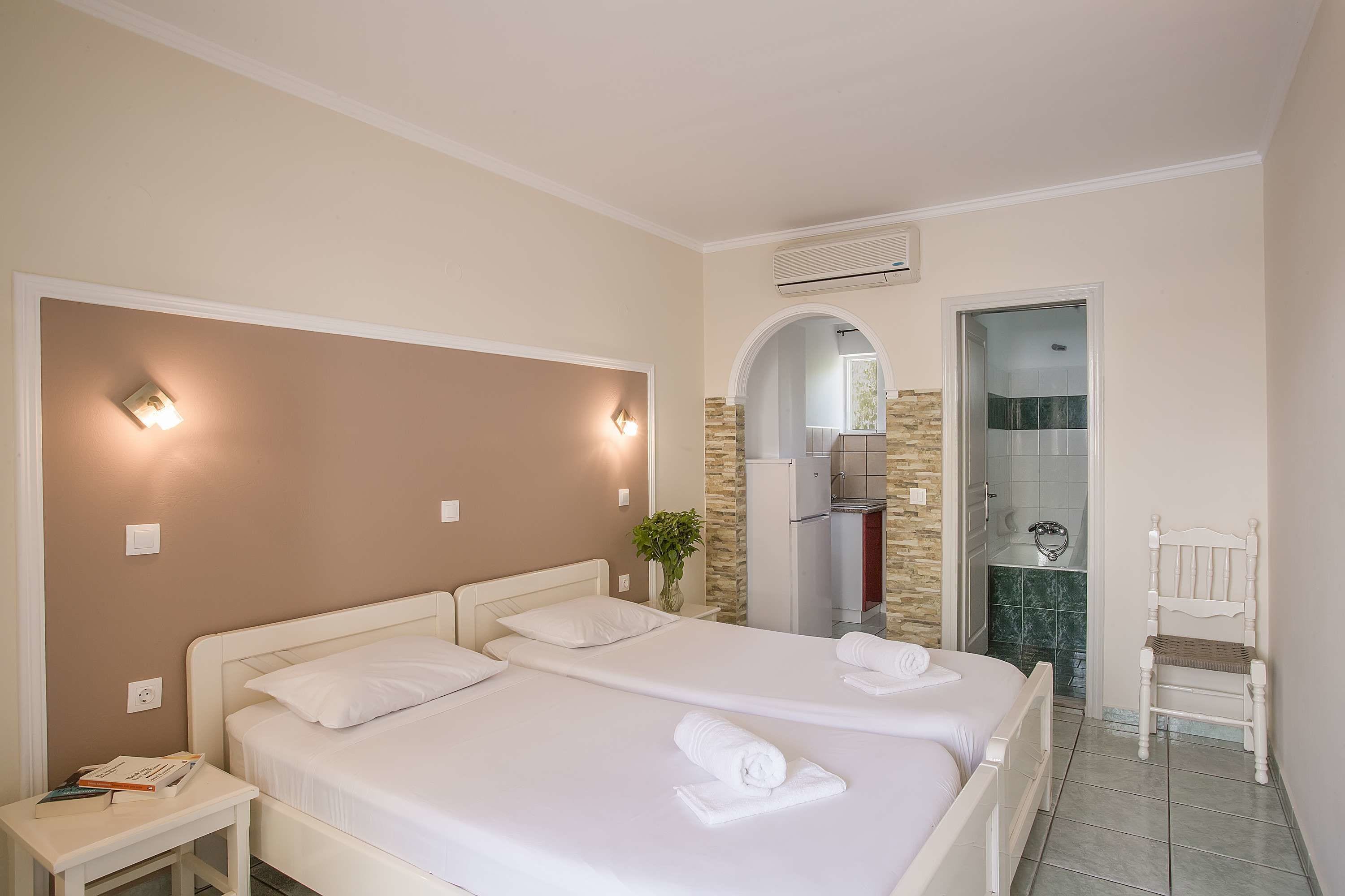 A hotel room with two beds, a small table, a chair, a mirror, and a bathroom visible through an archway.