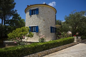 A stone tower with blue shutters, surrounded by lush greenery and flowers. - Mathraki Resort (Corfu)