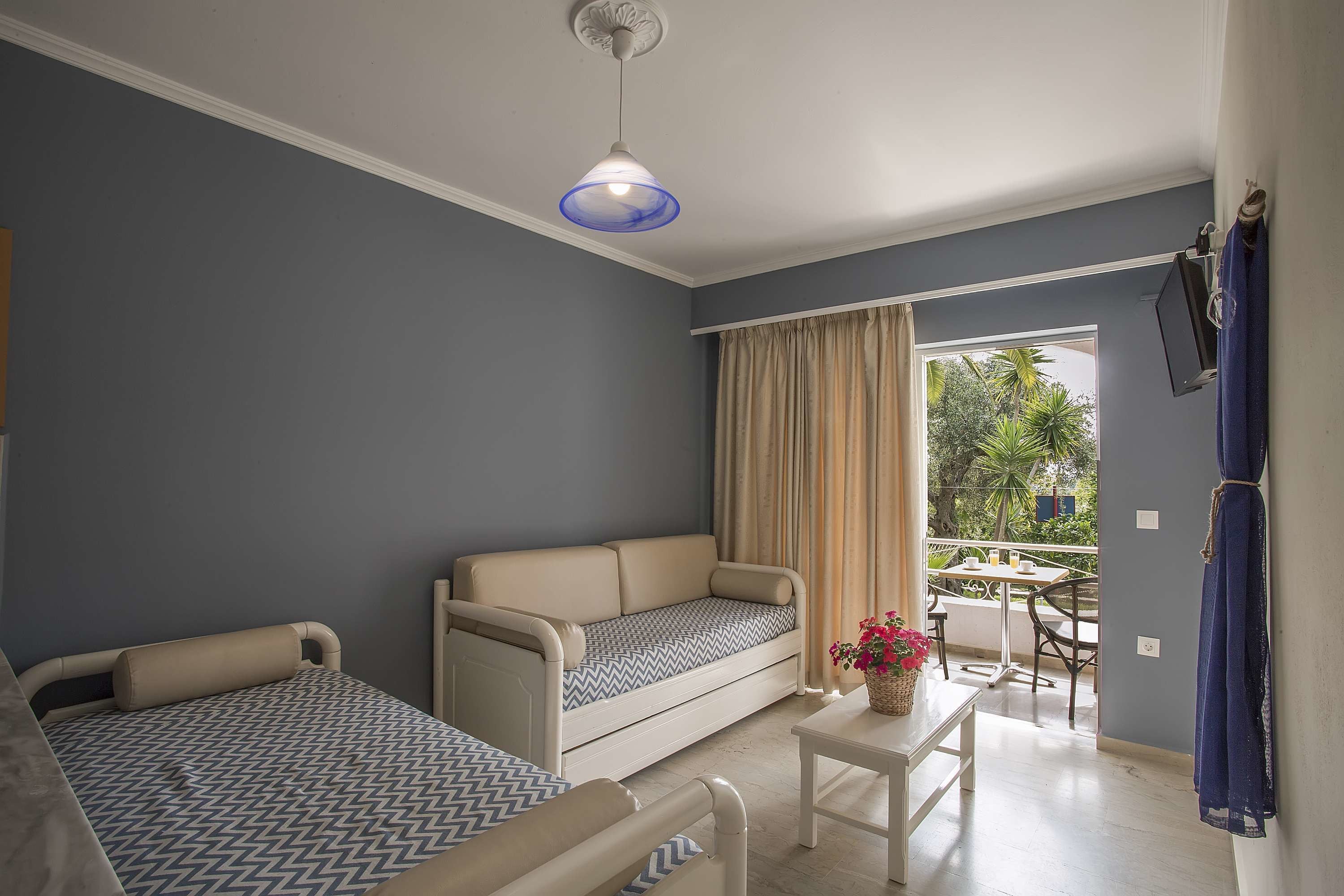 Una habitación con sofá, cama, una mesita con un florero y un balcón con mesa y sillas.