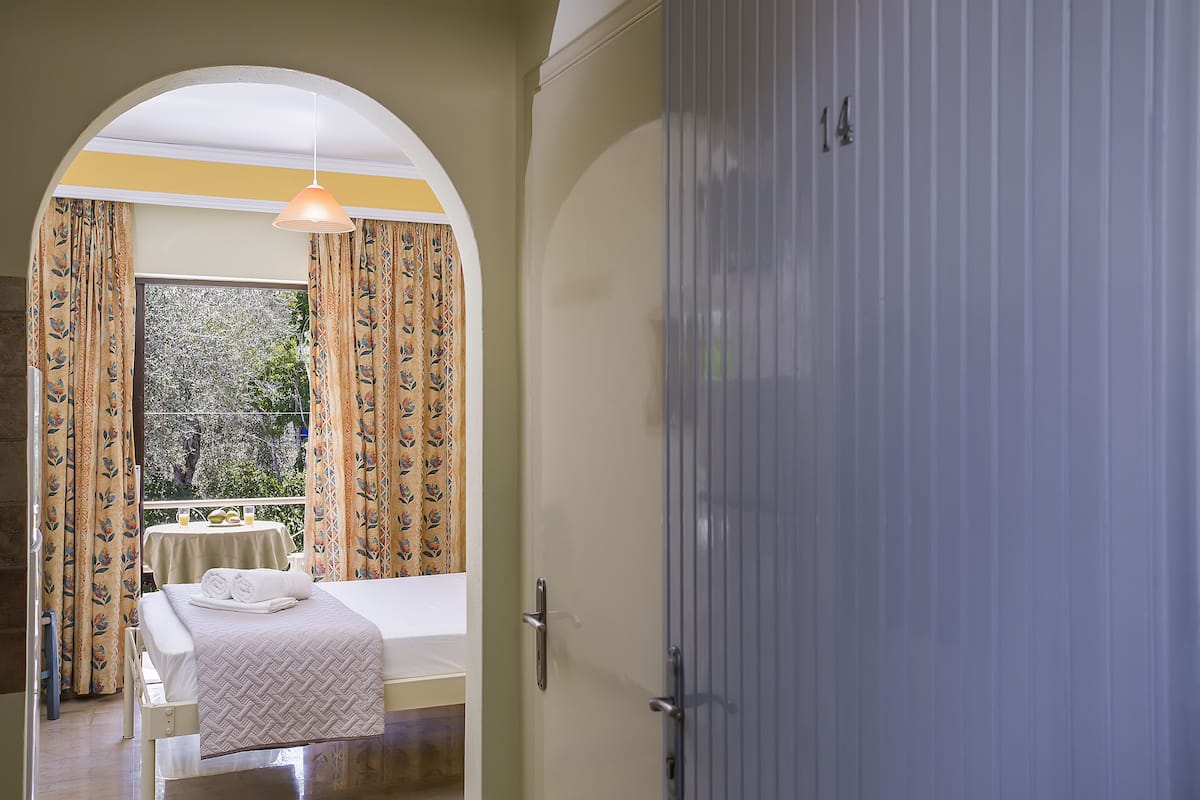 Quarto de hotel com uma cama, uma mesa com uma cadeira e vista para árvores pela janela.