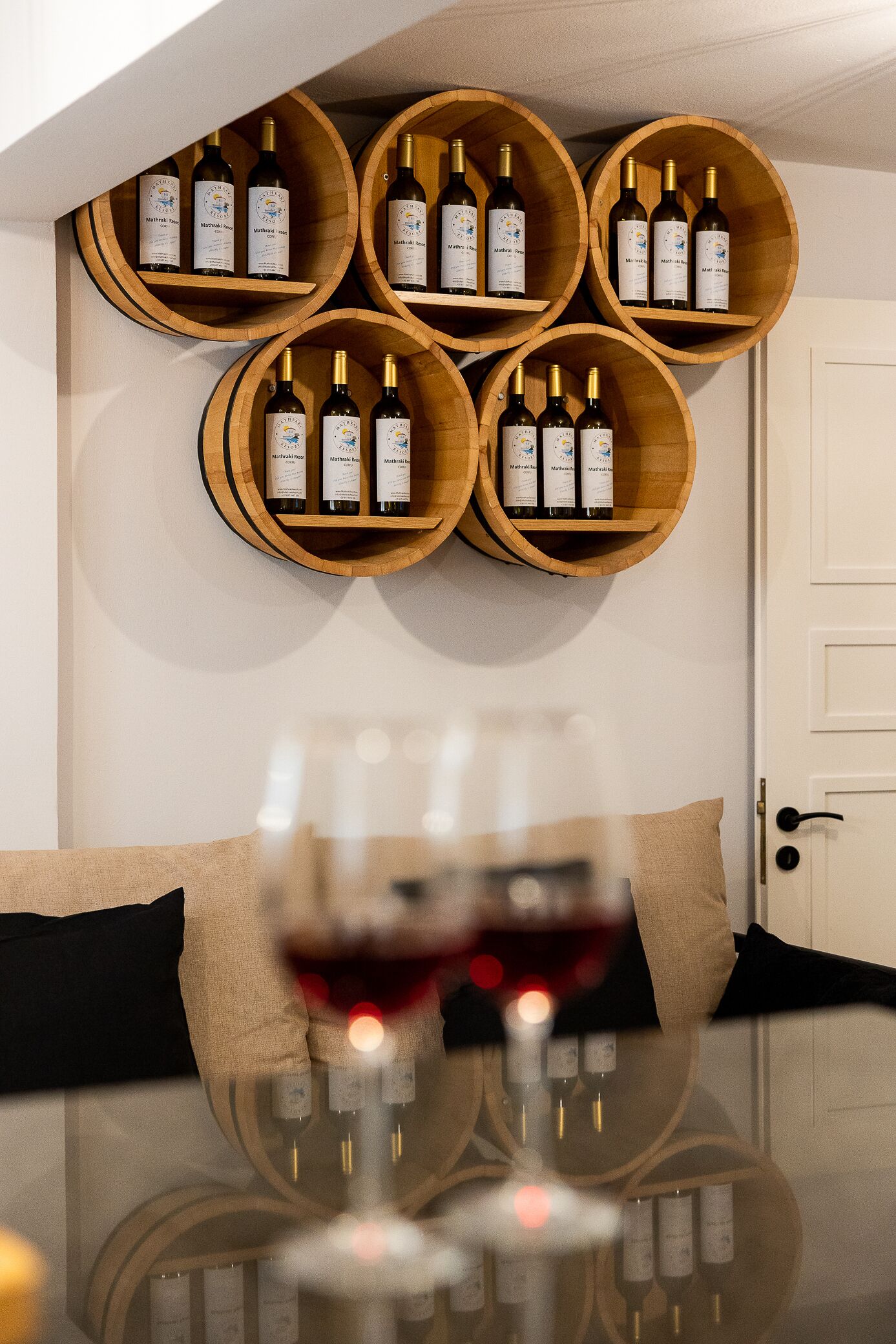 Una estantería con botellas de vino, una copa de vino tinto y un reflejo sobre una mesa de vidrio.