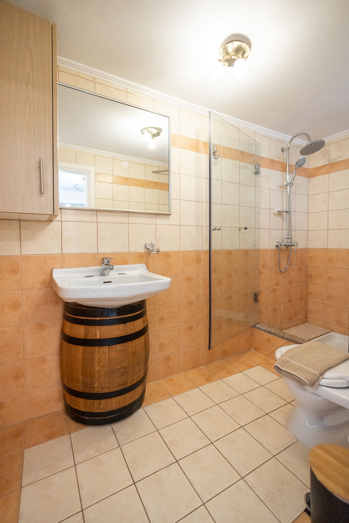 A bathroom with a wooden barrel sink, a glass-enclosed shower, and a toilet with a towel on it.