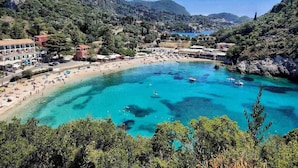 A coastal town with a beach, clear blue waters, and surrounding hills. - Mathraki Resort (Corfu)