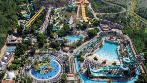 An aerial view of a resort with multiple water slides, pools, and a large central pool area surrounded by lounge chairs and umbrellas. - Mathraki Resort (Corfu)