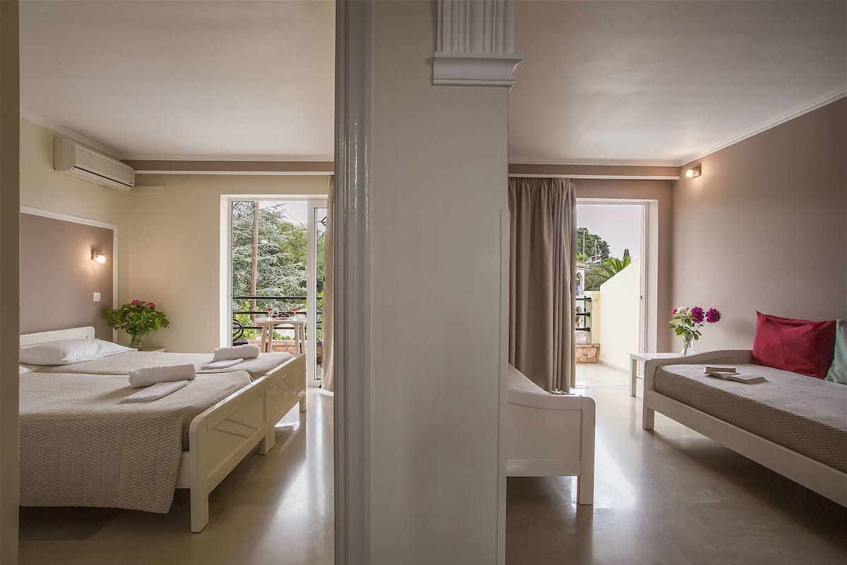 Quarto de hotel com duas camas, um sofá, uma mesinha e uma varanda com vista para vegetação.