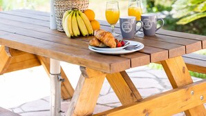 A wooden picnic table with a basket of flowers, a plate of food, and two mugs. - Mathraki Resort (Corfu)