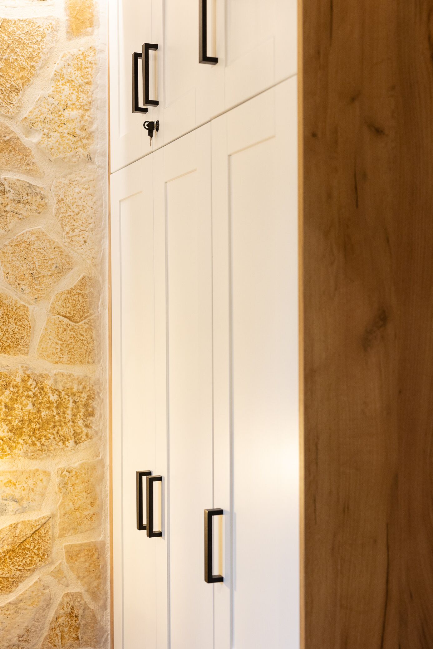 A white wardrobe with black handles against a stone wall.