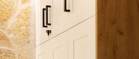 A white wardrobe with black handles against a stone wall.