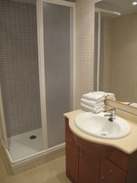 Un baño con ducha, lavamanos y toallas apiladas.