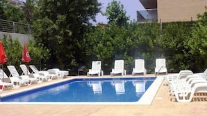 Ein Schwimmbecken mit weißen Liegestühlen und roten Flaggen, umgeben von viel Grün.