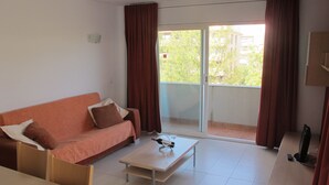 Ein Zimmer mit einer Couch, einem Couchtisch, einem Fernseher und einer Schiebetür zum Außenbereich.