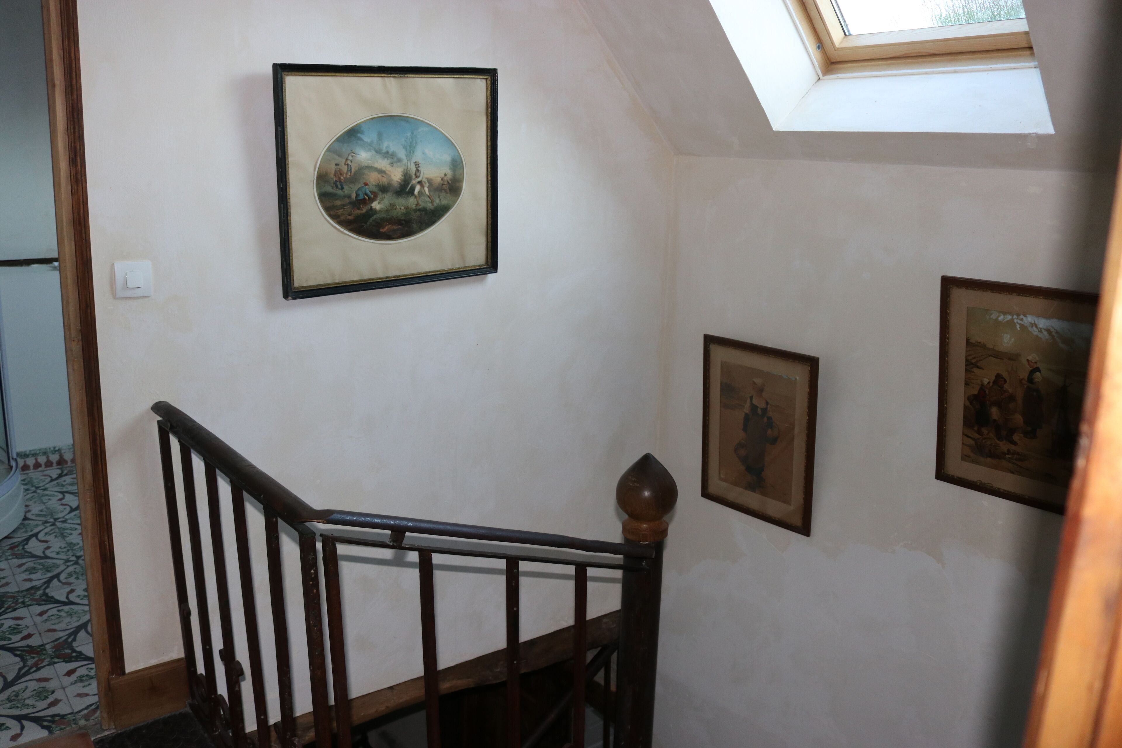 A staircase with a wooden handrail, a skylight, and three framed pictures on the wall.