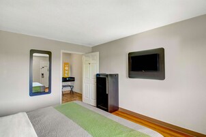 A hotel room with a bed, a small desk, a mirror, a television, and a door leading to another room.