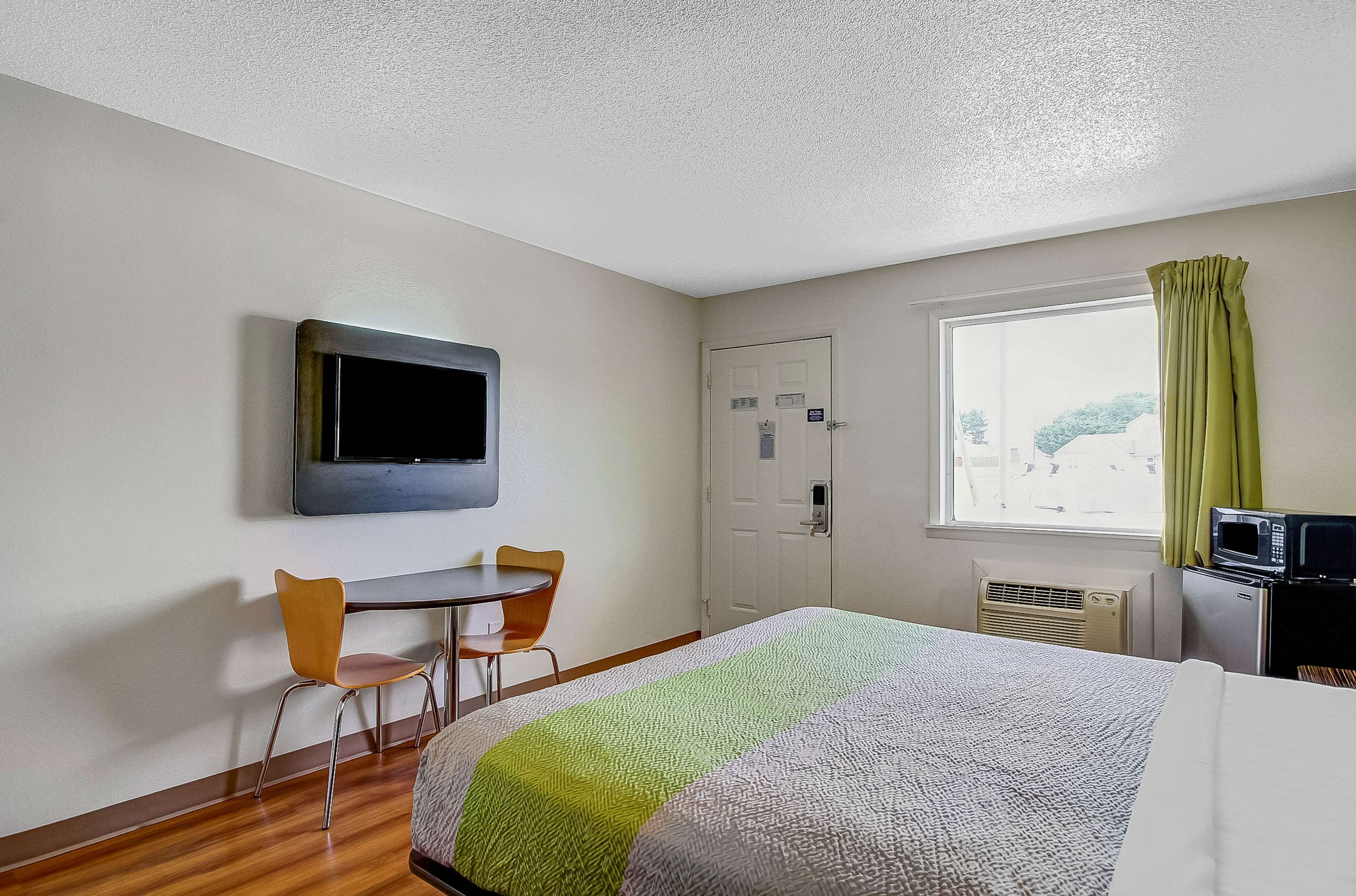 A hotel room with a bed, a desk with a chair, a television, a window with curtains, and a microwave.
