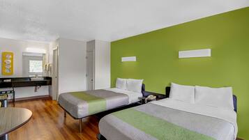 A hotel room with two beds, a desk, a chair, a bathroom, and a green accent wall.