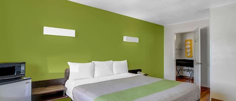 A hotel room with a bed, a microwave, a small refrigerator, and a green wall.