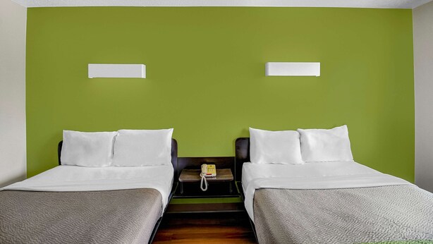 Ein Hotelzimmer mit zwei Betten, einem kleinen Tisch mit Telefon und grünen Wänden.
