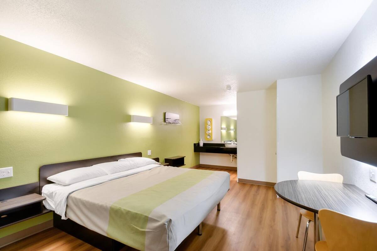 Hotelkamer met een bed, nachtkastjes, een bureau met stoel, een televisie en een badkamer met spiegel en wastafel.