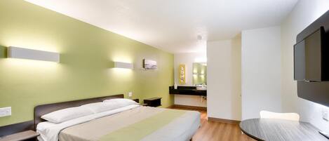 A hotel room with a bed, bedside tables, a desk with a chair, a television, and a bathroom with a mirror and sink.