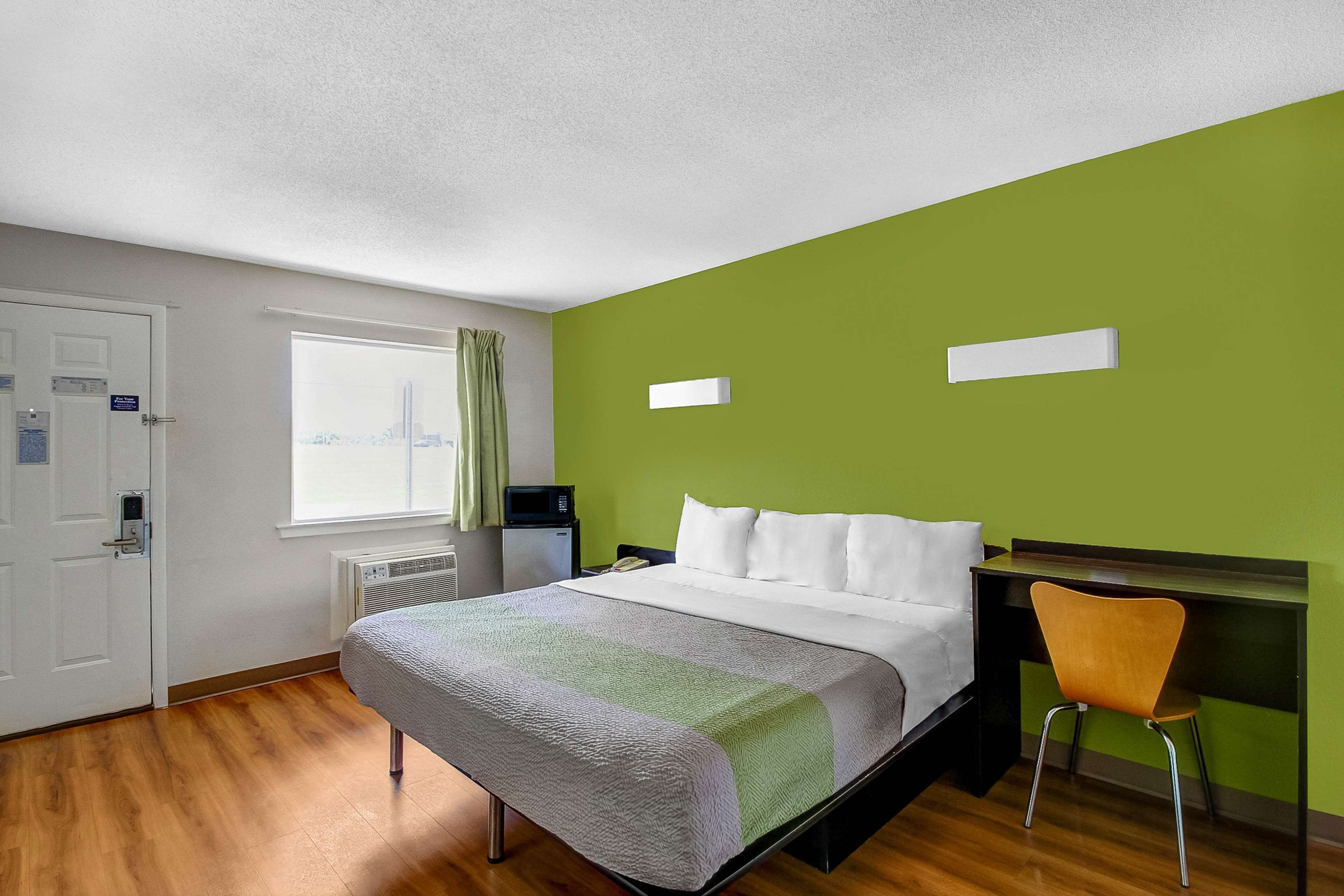 A hotel room with a bed, a desk, a chair, a window, and a door.