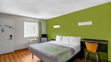 A hotel room with a bed, a desk, a chair, a window, and a door.