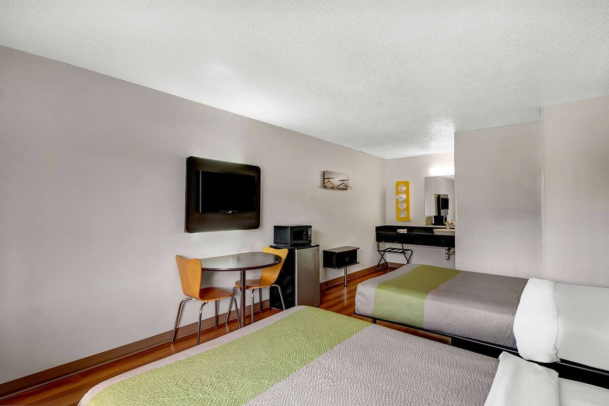 Hotelkamer met twee bedden, een bureau met stoel, een magnetron, een klein tafeltje en een aan de muur bevestigde televisie.