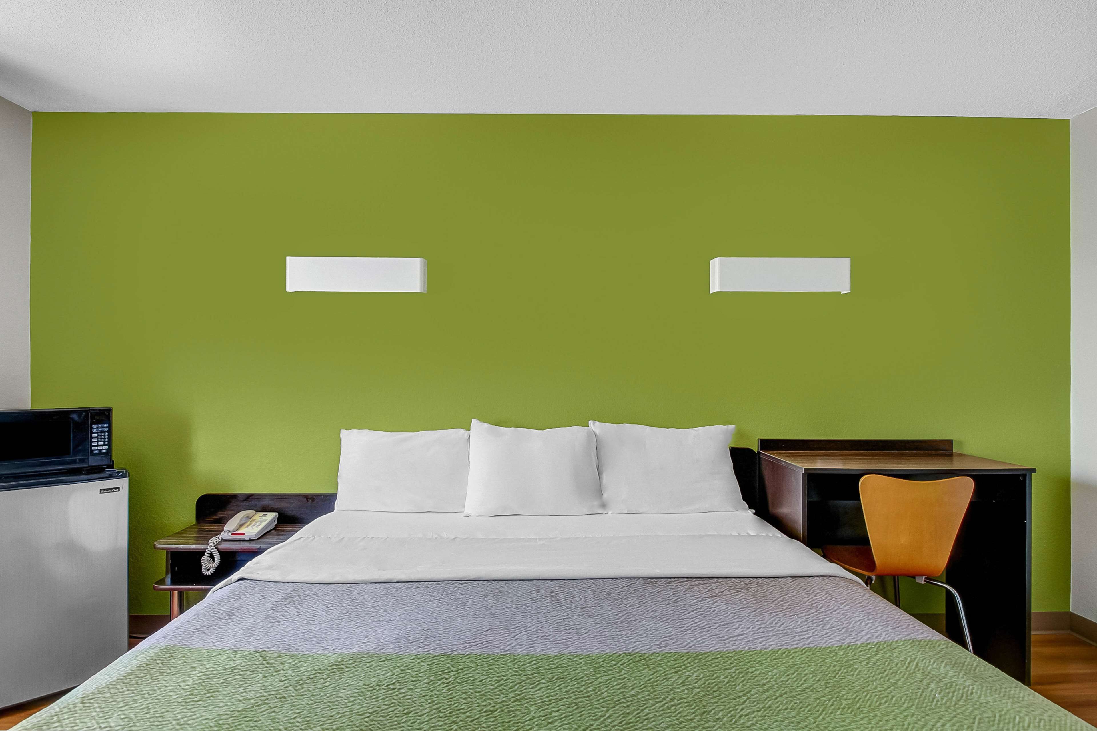 Una habitación de hotel con cama, escritorio, silla, microondas y teléfono.