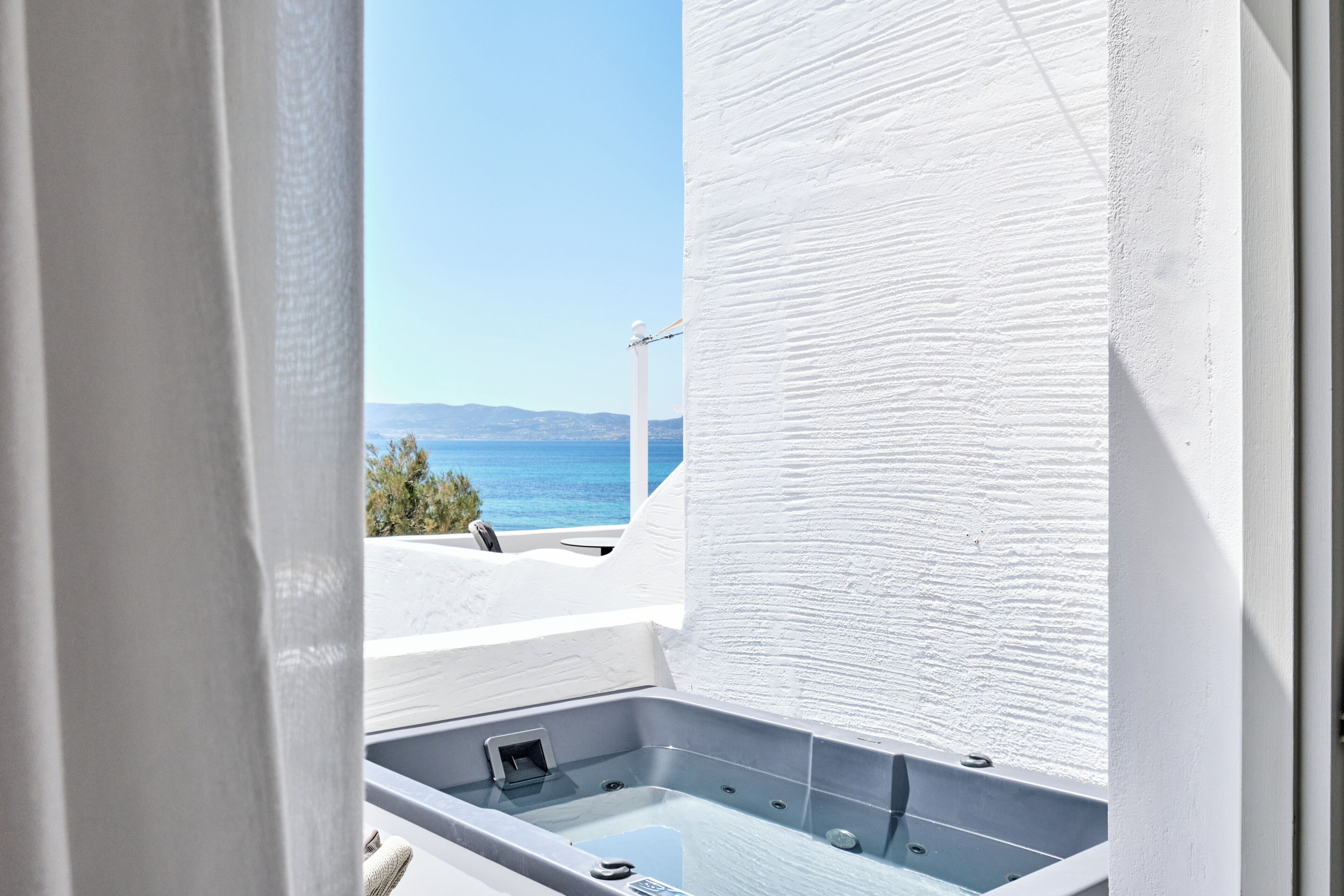 A balcony with a hot tub, a view of the sea, and a white textured wall.