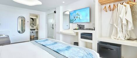 Ein modernes Hotelzimmer mit einem großen Bett, einem an der Wand montierten Fernseher, einer Holzbalkendecke und einem Kleiderständer mit Bademänteln.