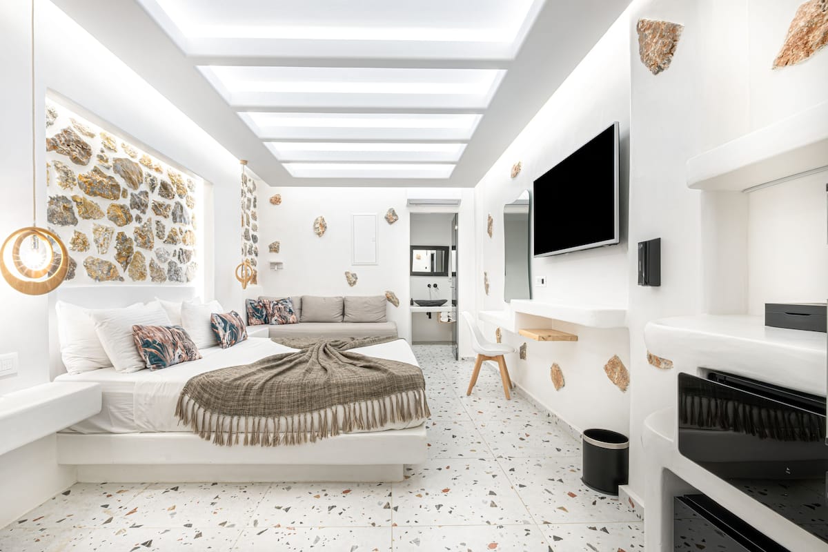 A modern bedroom with a bed, a sofa, a TV, and a piano.