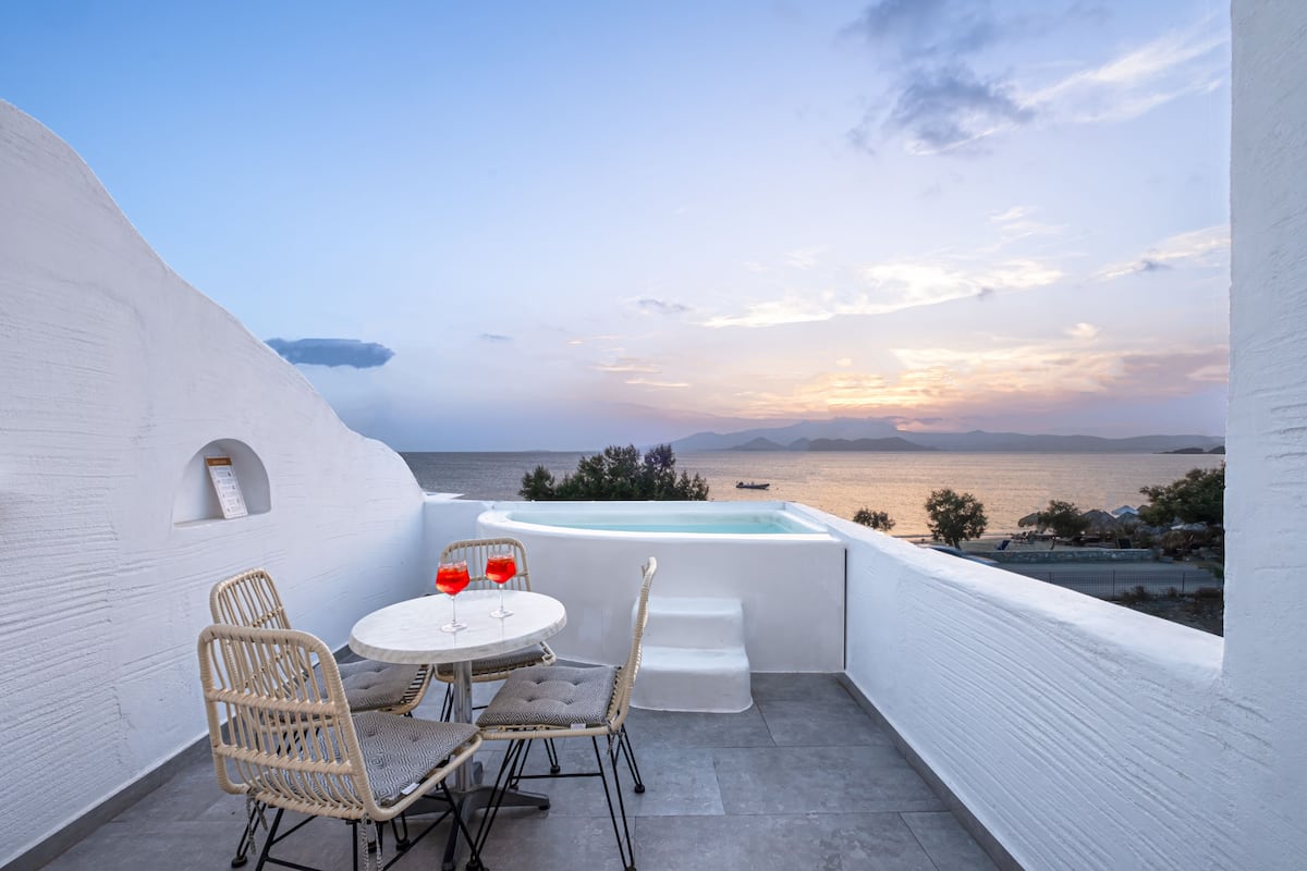 A terrace with a white wall, a round table with wicker chairs, a small white table, and a hot tub.