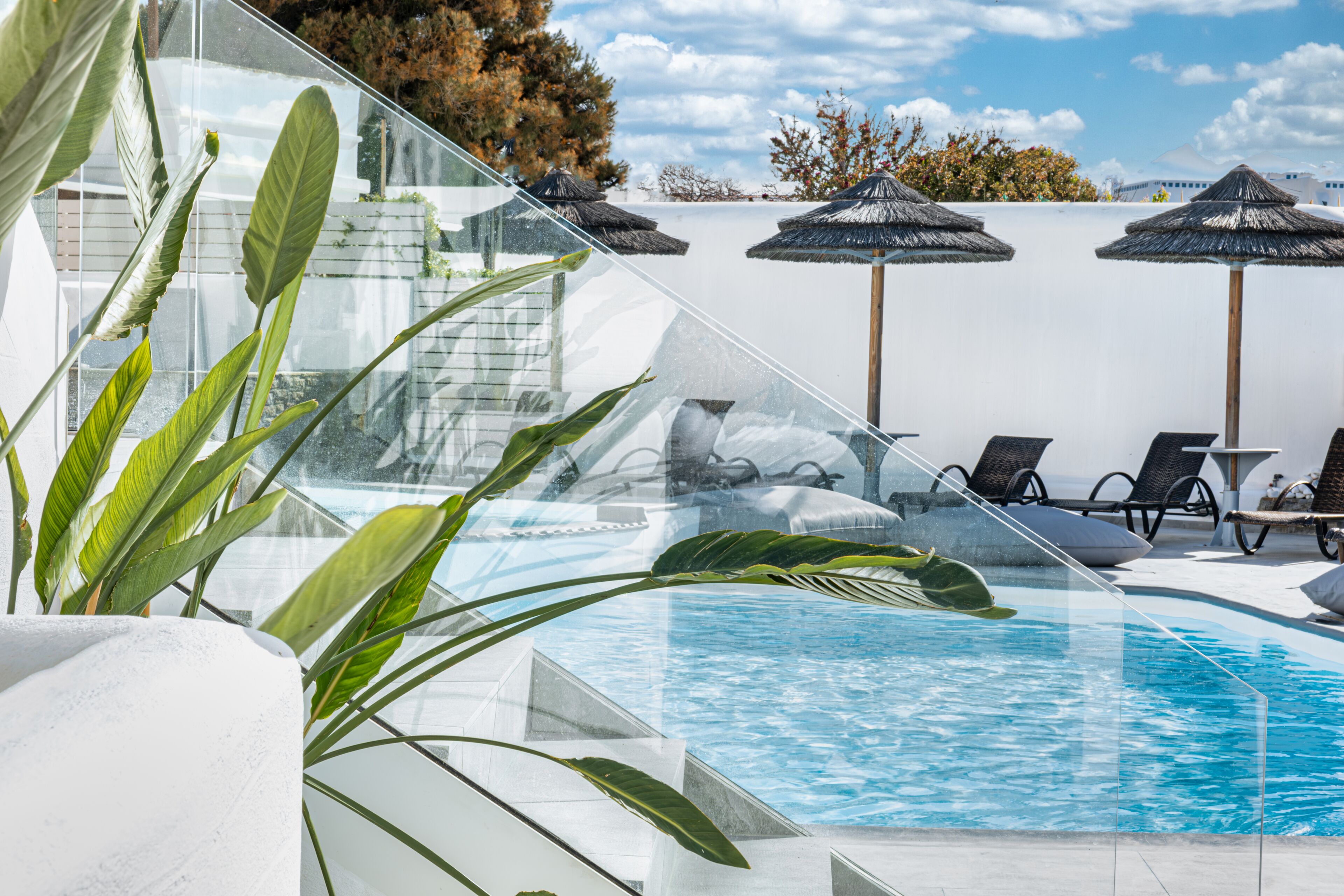Un área de piscina con paredes de vidrio transparente, sillones de descanso y sombrillas.