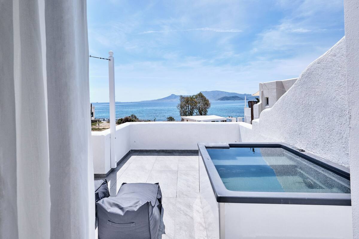 A rooftop terrace with a pool, white walls, and a view of the sea and mountains.