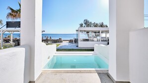 A pool area with a view of the sea, white pillars, and outdoor furniture.