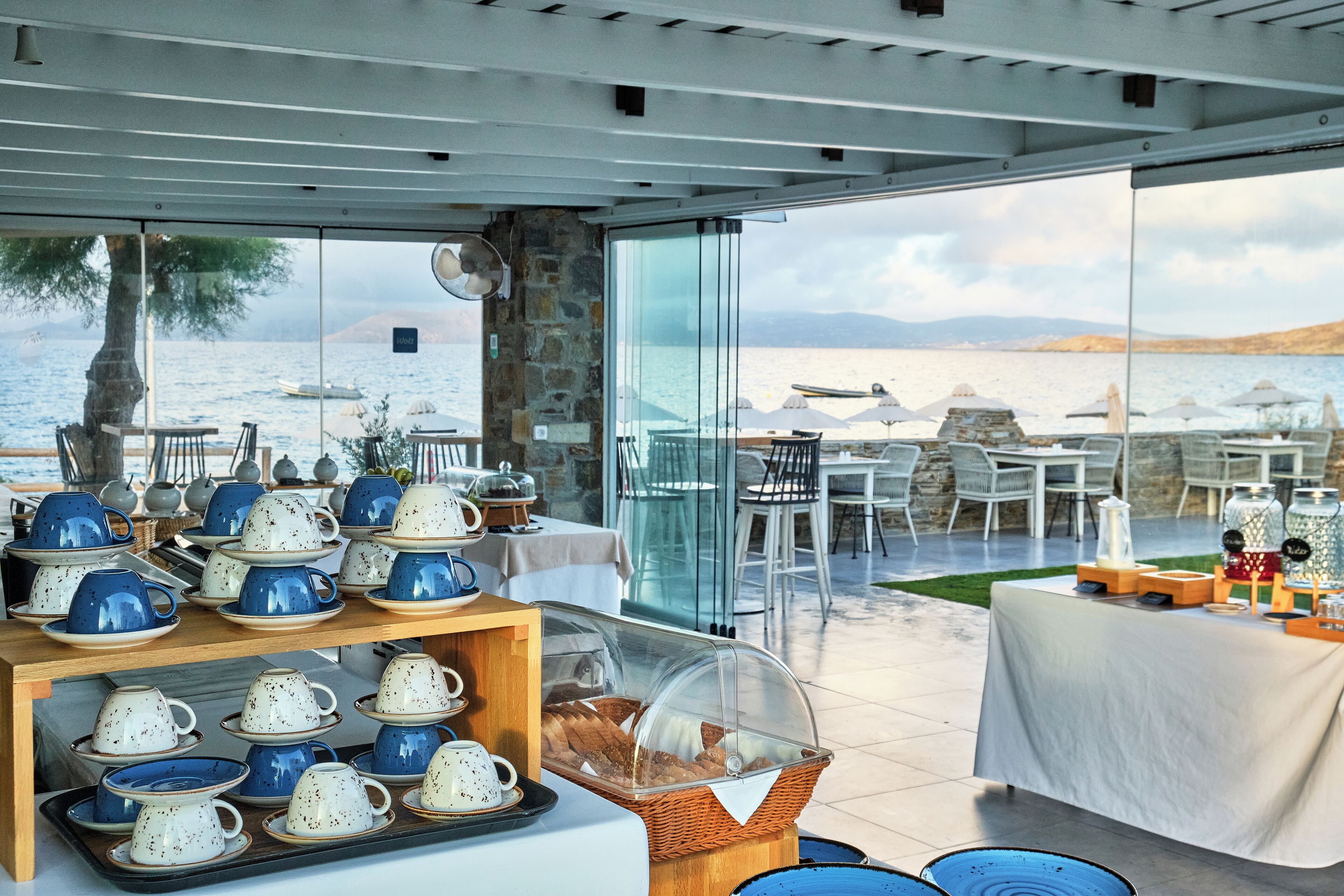 Een restaurant aan de kust met terras, met uitzicht op zee, met een buffet en aardewerk schalen en een rieten mand met brood.