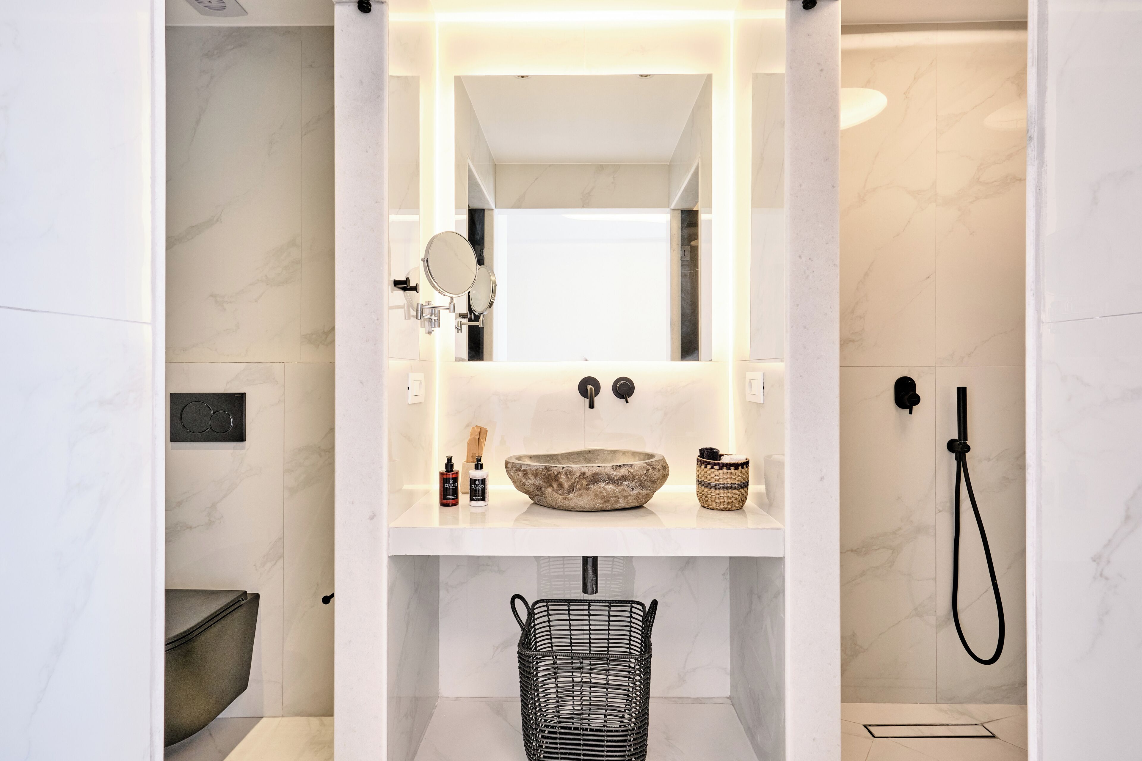 Une salle de bain moderne avec un lavabo en marbre, un grand miroir, une douche et un panier en métal noir.